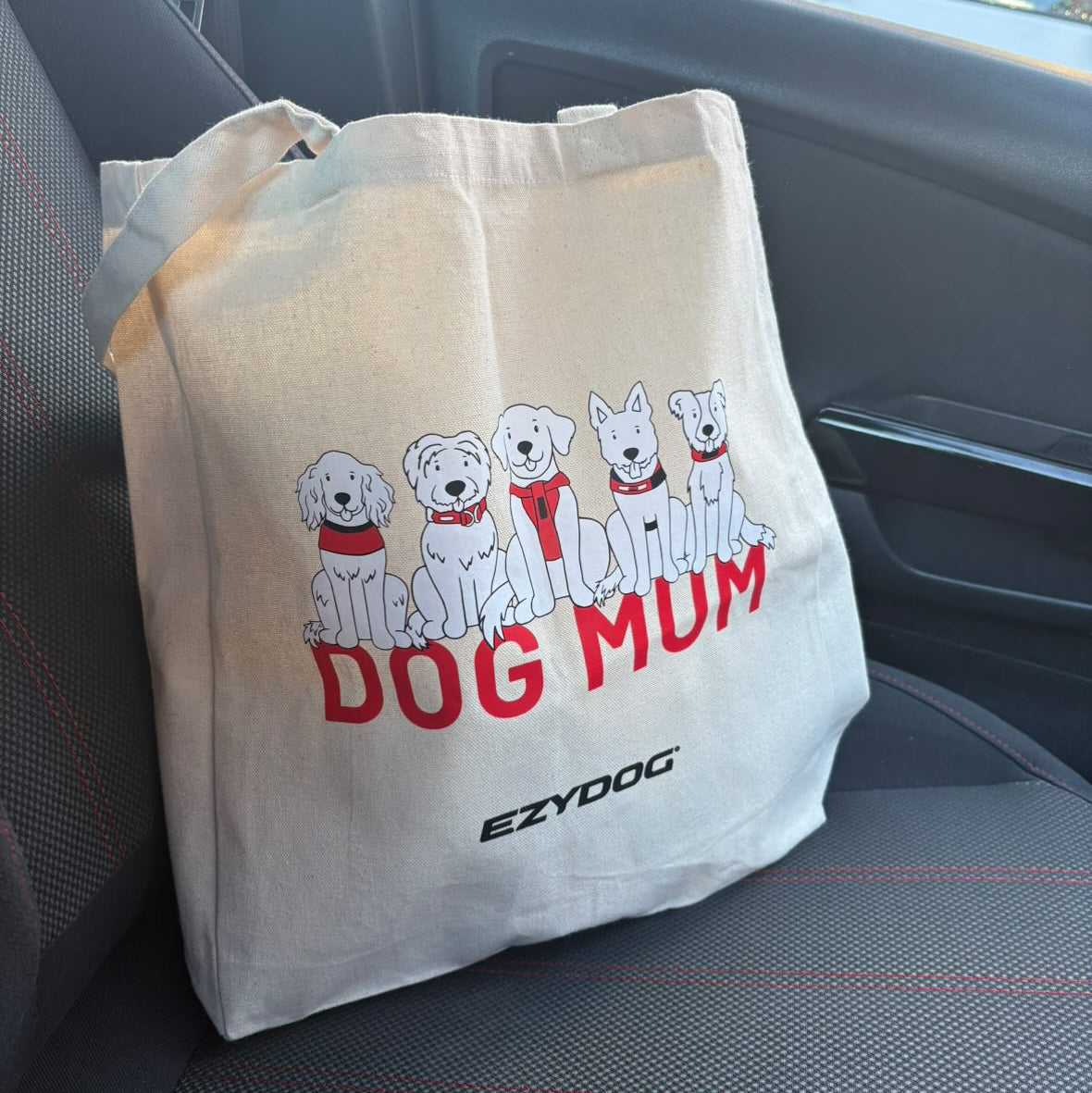 Beige tote bag with 'DOG MUM' and dog illustrations on a car seat.