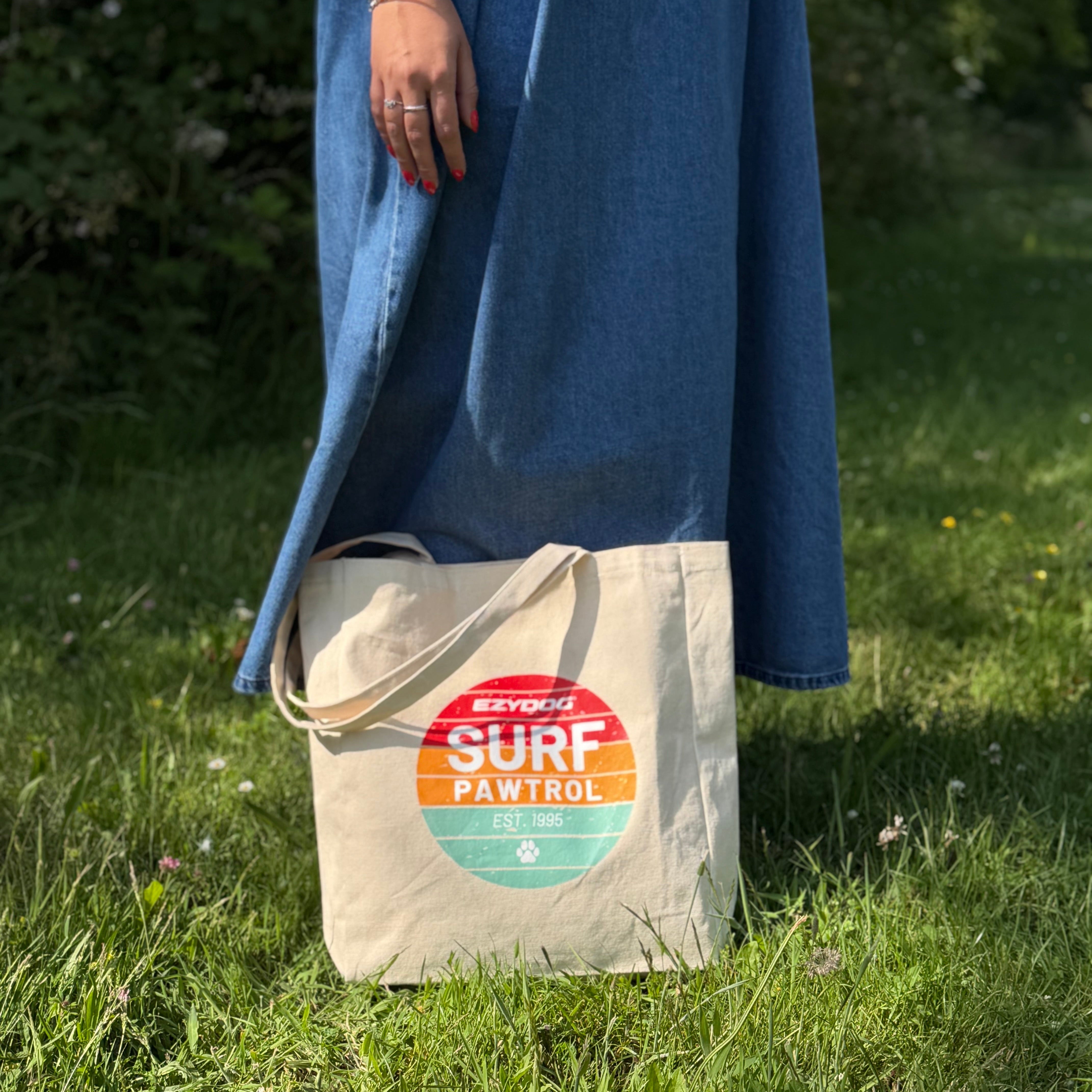 Person holding a tote bag with 'Surf Patrol' design on grass